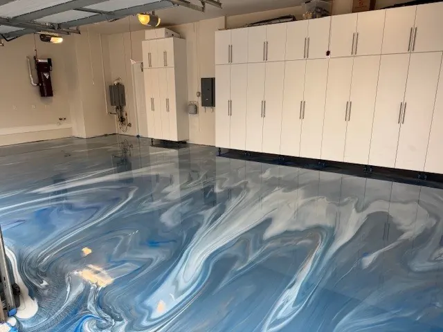 Blue and silver metallic epoxy garage floor beneath white storage cabinets